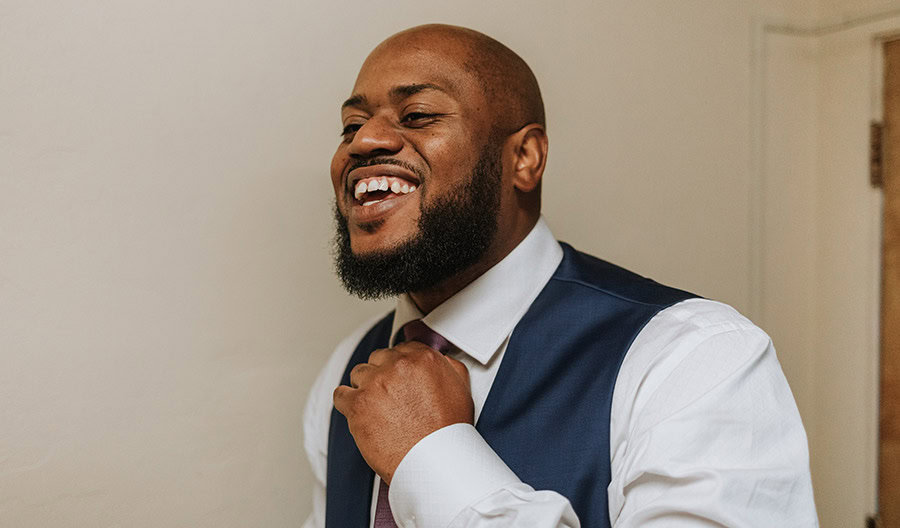 Man wearing a suit and fixing his tie while smiling.