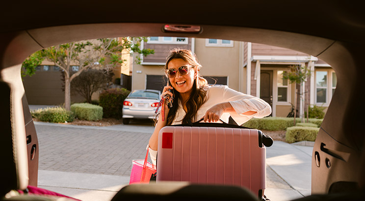 Woman putting a pink suitcase in the trunk of her car