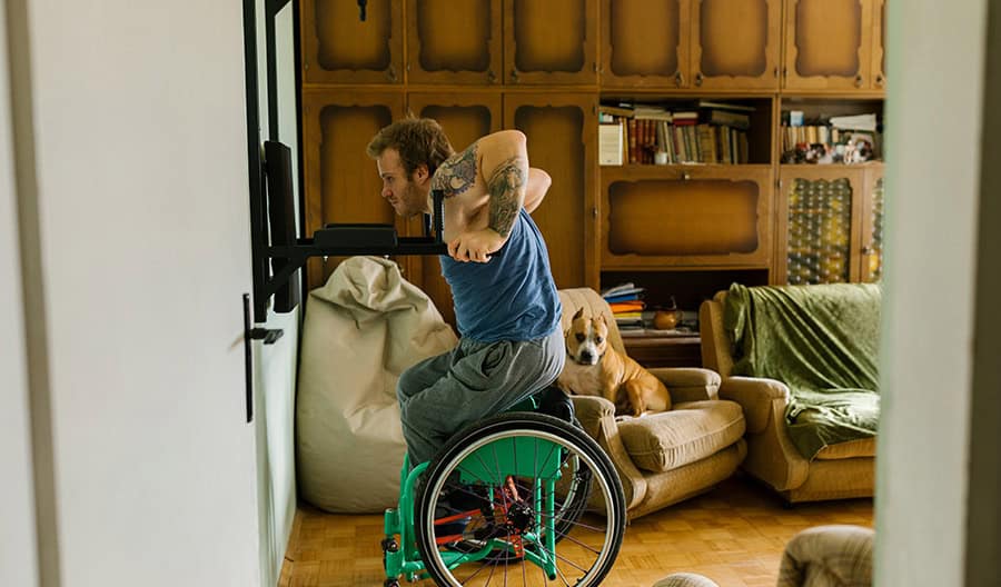Man in blue shirt pushing himself up from wheelchair on workout equipment.