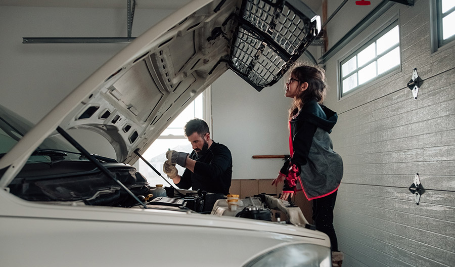 Young girl smiling while looking under the hood of a white truck.