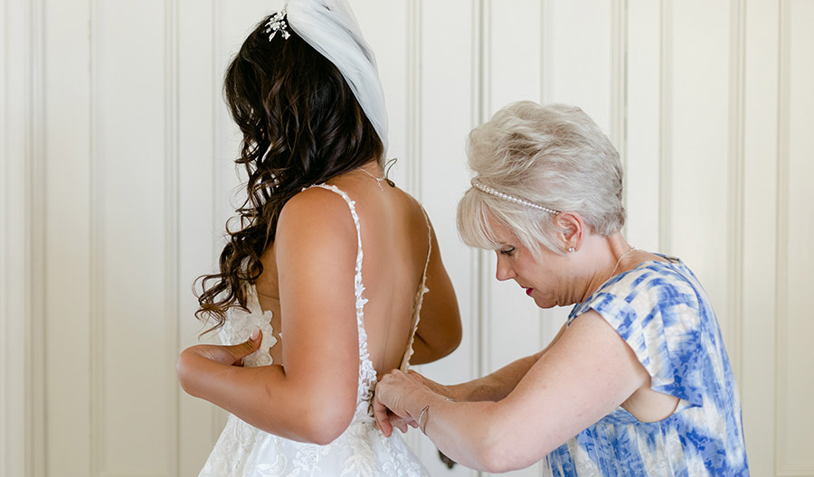 Woman helping young woman button her wedding gown